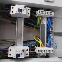 Wnętrze skrzynki elektrycznej z zamontowanymi dwoma wyłącznikami różnicowoprądowymi ABL RP2203, listwami zaciskowymi i uporządkowanymi przewodami o różnych kolorach (niebieski, żółty, zielony...