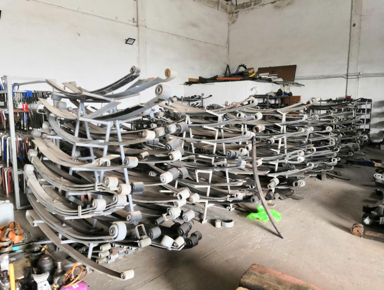 Stos zwiniętych resorów samochodowych w warsztacie, widoczne narzędzia i elementy wyposażenia warsztatowego w tle.