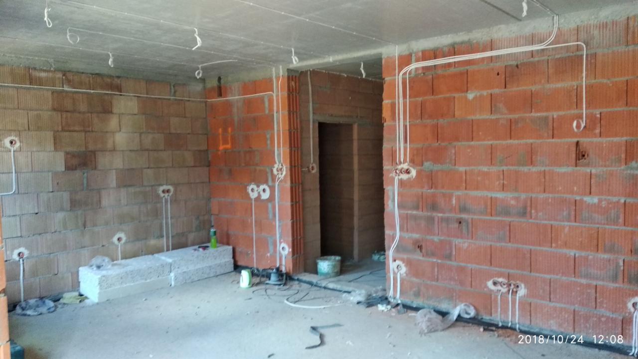 Surowy stan instalacji elektrycznej w nowym budynku: przewody wyprowadzone ze ścian z cegły, puszki instalacyjne zamontowane, widoczne przewody na suficie, brak osprzętu.