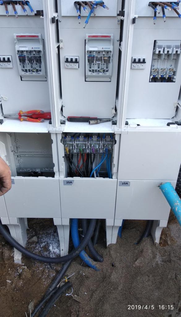 Rozdzielnica elektryczna w trakcie montażu, widoczne zabezpieczenia, przewody, peszle, narzędzia i fragment dłoni elektryka