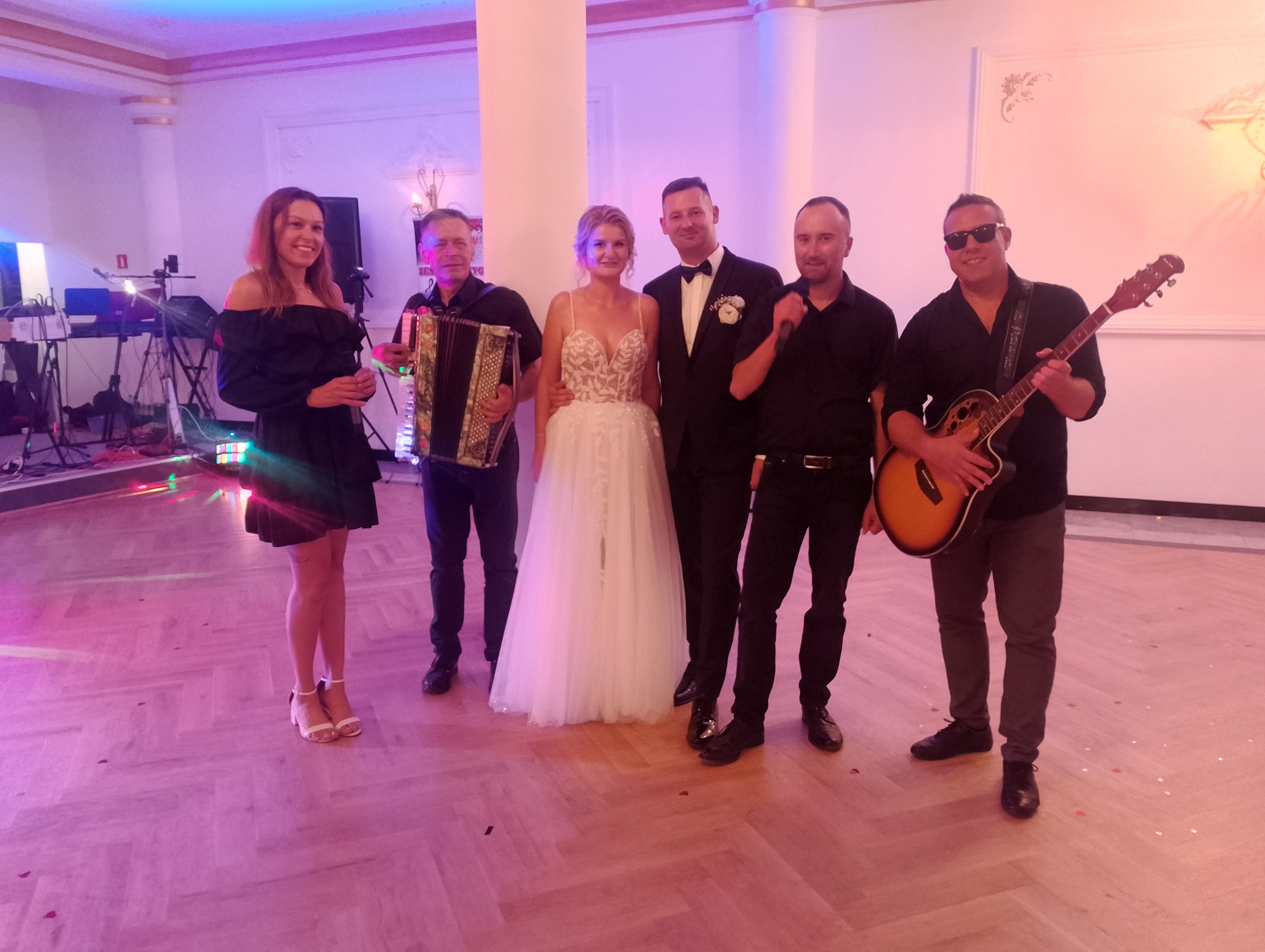 Zespół muzyczny z Jaktorowa pozuje do zdjęcia z parą młodą w eleganckiej sali weselnej, akordeon, gitara akustyczna i mikrofony w tle.