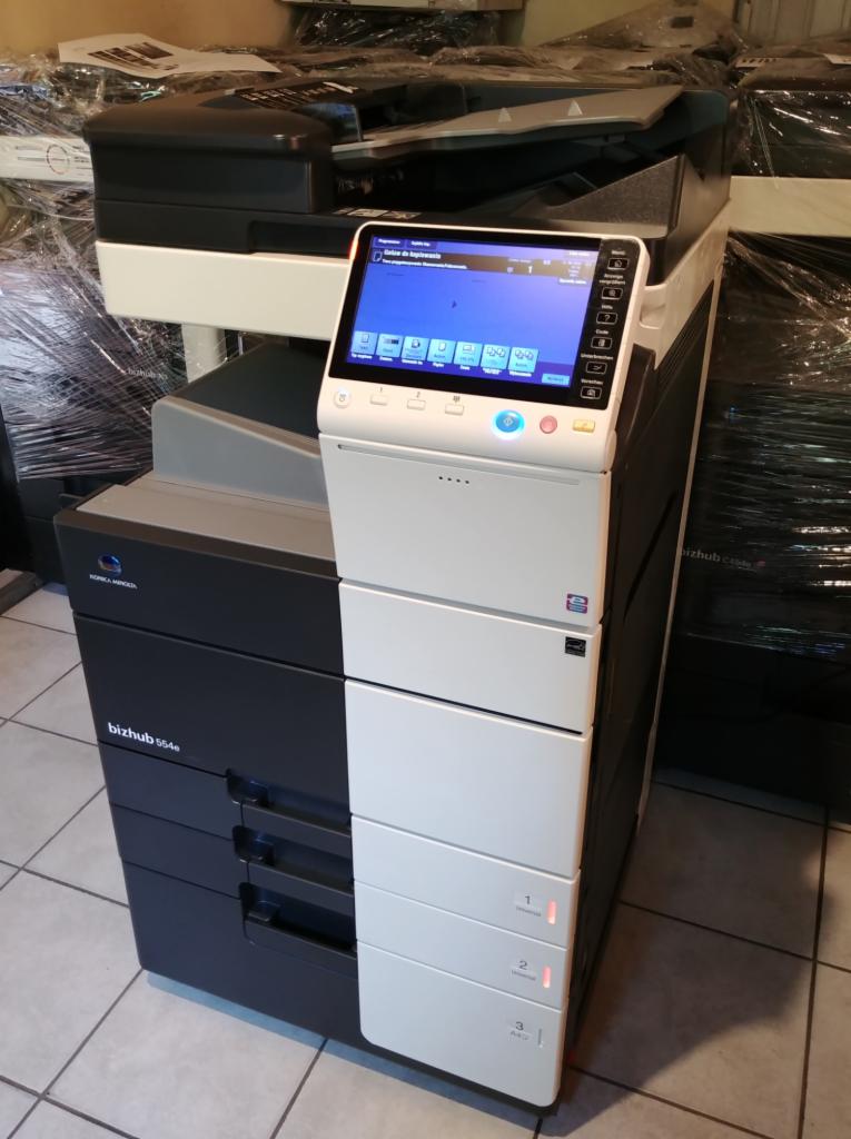 Nowa, wielofunkcyjna kserokopiarka Konica Minolta bizhub 554e z dotykowym panelem sterowania, widoczne trzy szuflady na papier z oznaczeniami formatów, ustawiona na kafelkach.