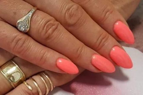 Dłoń z koralowymi, migdałowymi paznokciami i złotymi pierścionkami, w tym pierścionkiem zaręczynowym z brylantem.