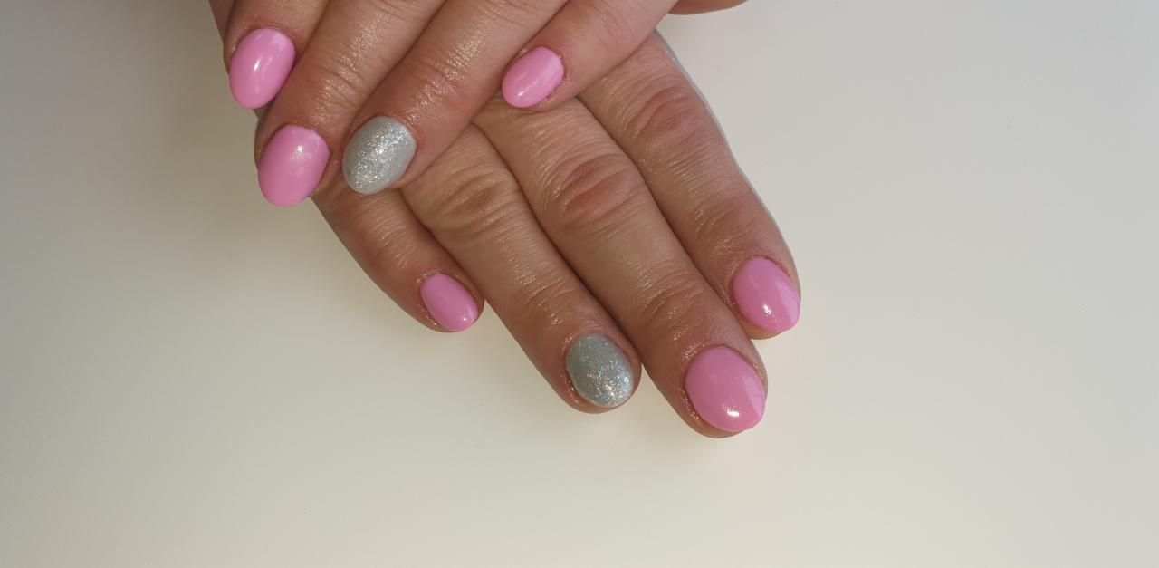 Dłonie z pomalowanymi paznokciami w odcieniach różu i srebrnego brokatu, wykonane w salonie w Wejherowie. Widoczne delikatne skórki i błyszczący lakier.