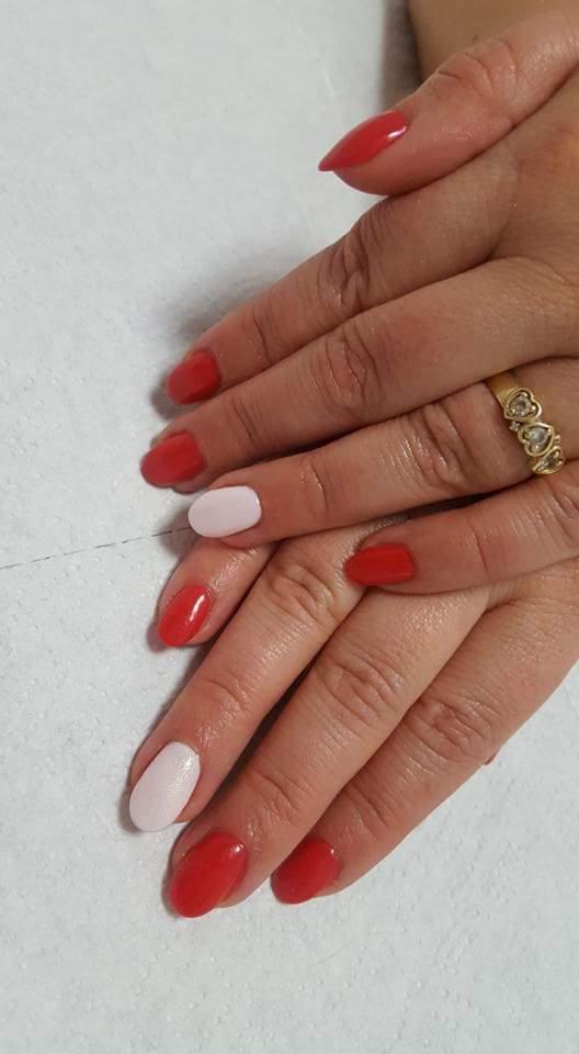 Dłonie z czerwono-białym manicure hybrydowym, pierścionek z trzema sercami na serdecznym palcu, na białym tle.