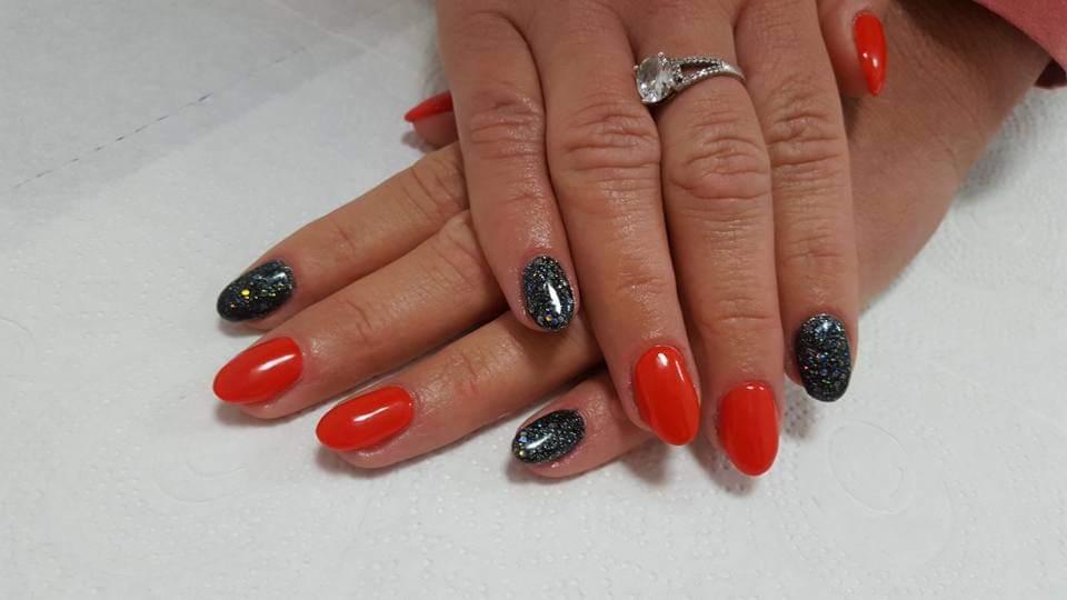 Dłonie z czerwonymi i brokatowymi paznokciami na białym tle, pierścionek z dużym oczkiem na palcu serdecznym.