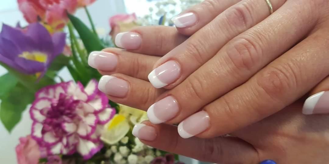 Dłonie z klasycznym, jasnoróżowym manicure francuskim na tle bukietu kolorowych kwiatów.