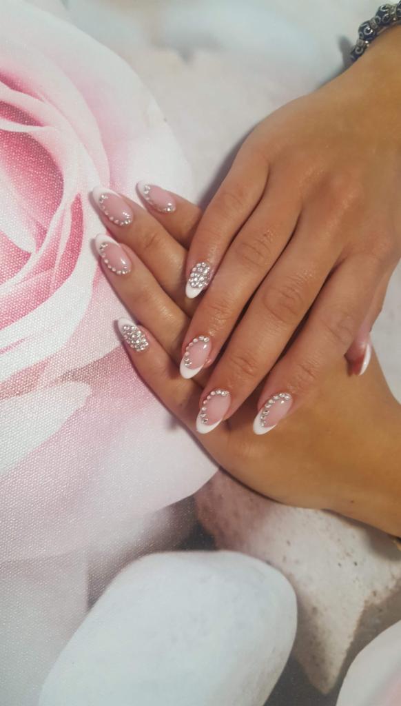 Dłonie z owalnym manicure francuskim ozdobionym drobnymi kryształkami na tle wzoru z różowych róż.