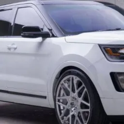 Biały SUV z przyciemnionymi szybami bocznymi i tylną, chromowanymi felgami, oraz czarnym dachem, zaparkowany na szarym tle.