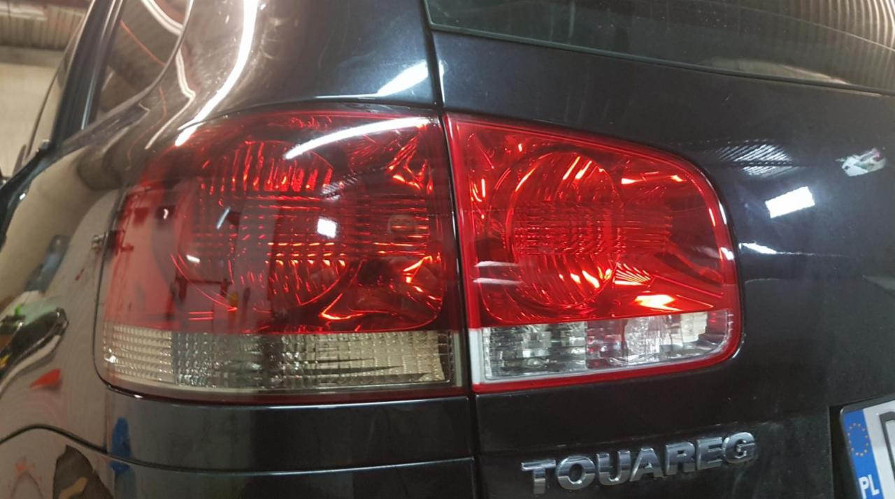 Czerwone, tylne światła samochodu Touareg, po zabiegu przyciemniania folią, widoczne z bliska. Na karoserii widoczne refleksy świetlne.