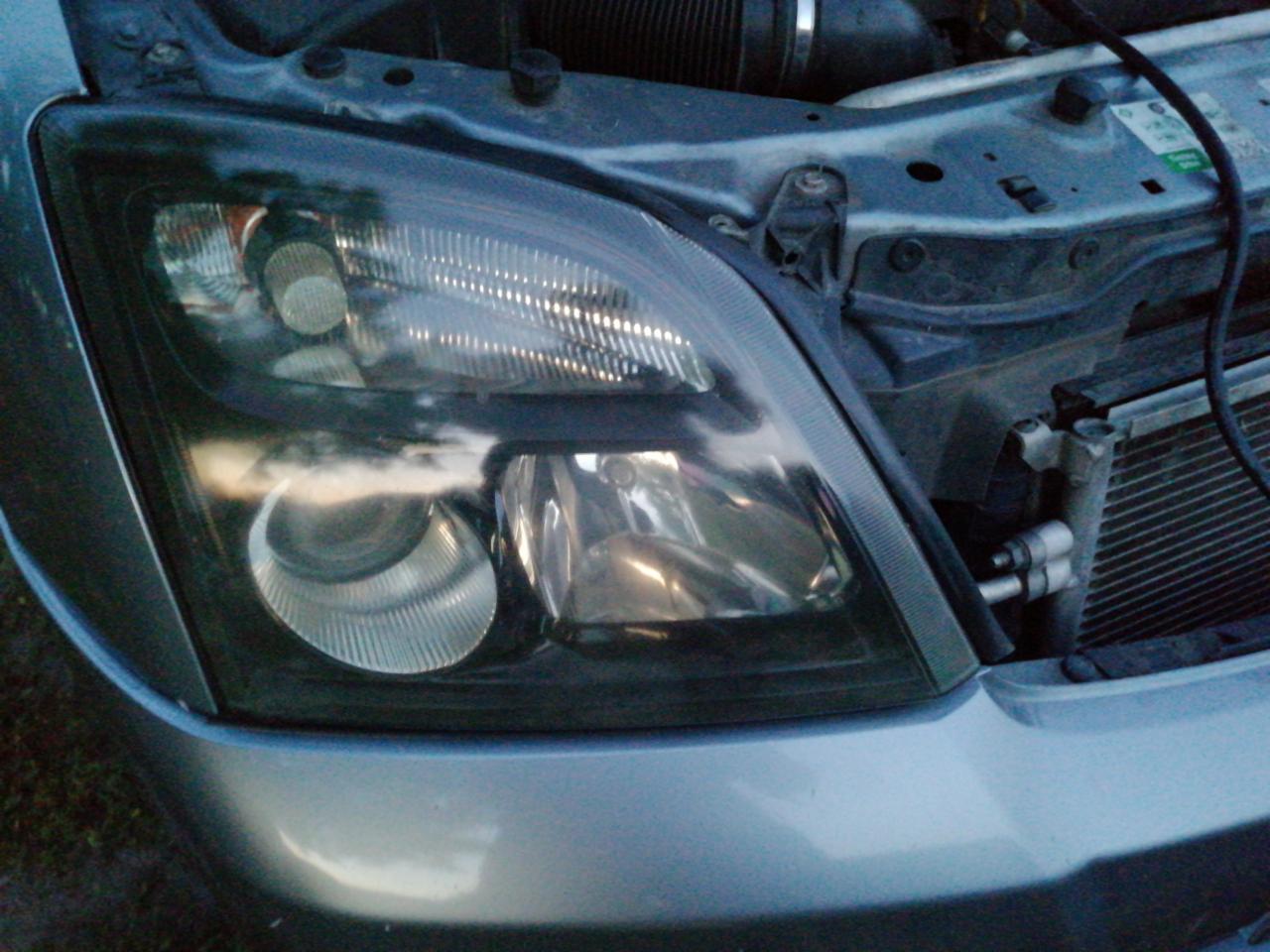 Reflektor samochodu po renowacji z widocznymi elementami silnika w tle.