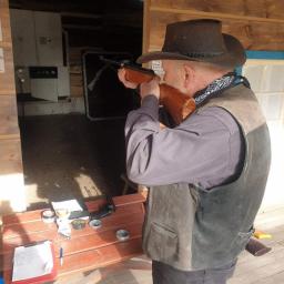 Sheriff Cordell - Mężczyzna w kapeluszu kowbojskim celuje z karabinu pneumatycznego w strzelnicy, na stole amunicja i notatnik.