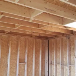 Wnętrze budynku w trakcie budowy, widoczne drewniane ramy ścian i sufitu, płyty OSB na ścianach, surowe drewno konstrukcyjne.