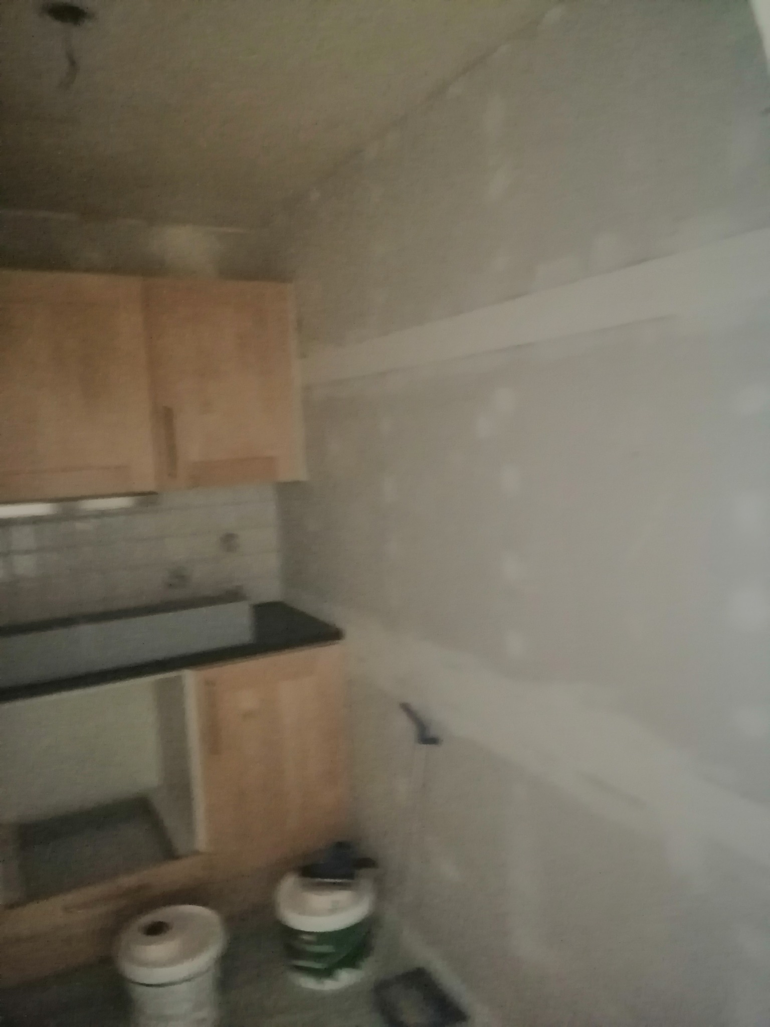 Wnętrze kuchni w trakcie remontu, ściany przygotowane do malowania, widoczne ślady szpachlowania, na podłodze puszki z farbą, zamontowane szafki kuchenne.