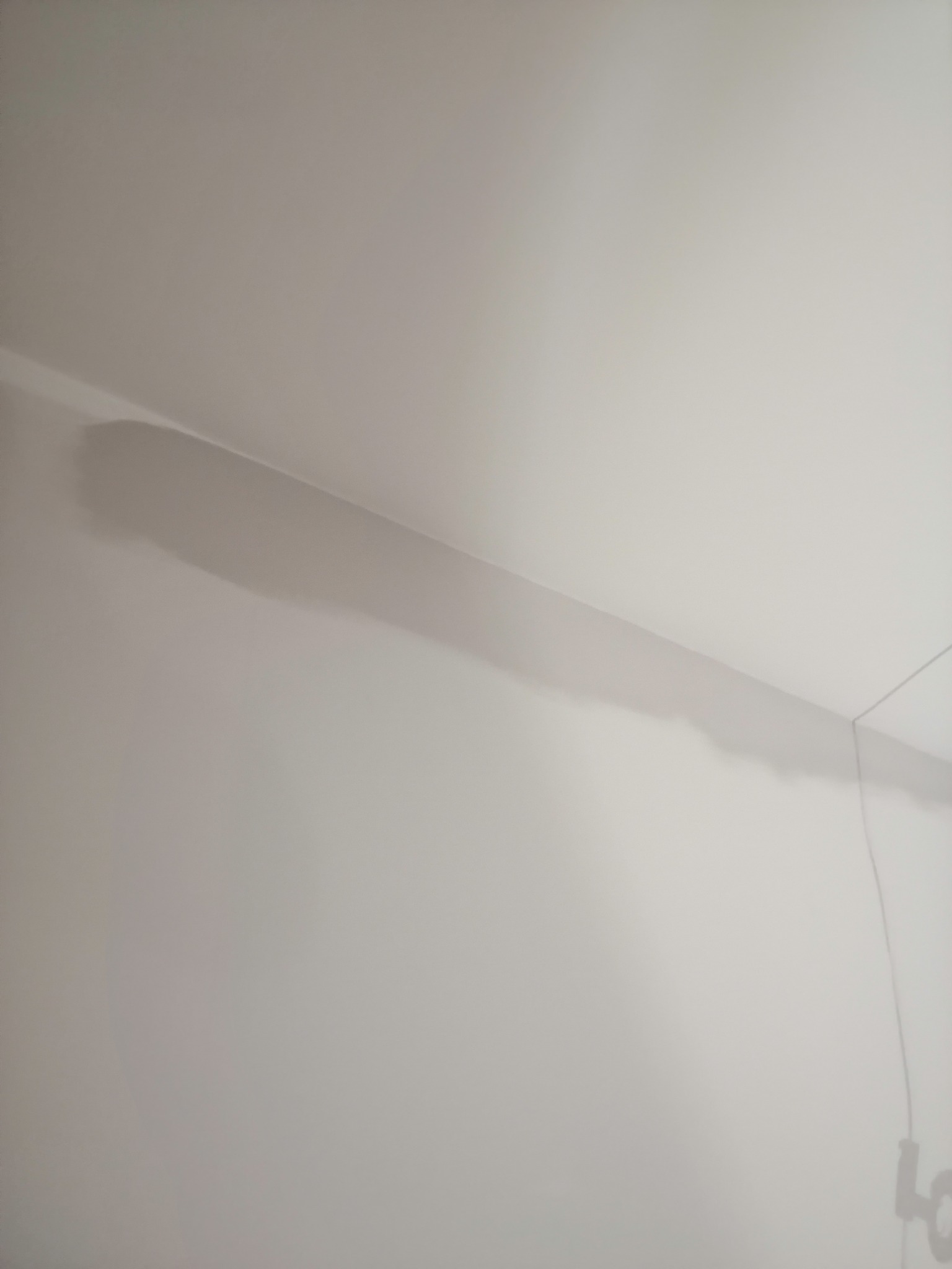 Świeżo pomalowany róg pokoju z widocznym, delikatnym cieniem listwy przysufitowej na gładkiej, białej ścianie.