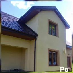 Elewacja domu jednorodzinnego w odcieniach beżu z brązowymi oknami, dachem z dach&oacute;wki i rynnami po renowacji, widok z dołu.