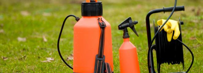 Opryskiwacz ciśnieniowy plecakowy, mniejszy opryskiwacz ręczny i zwinięty wąż z żółtą rękawicą na trawie.
