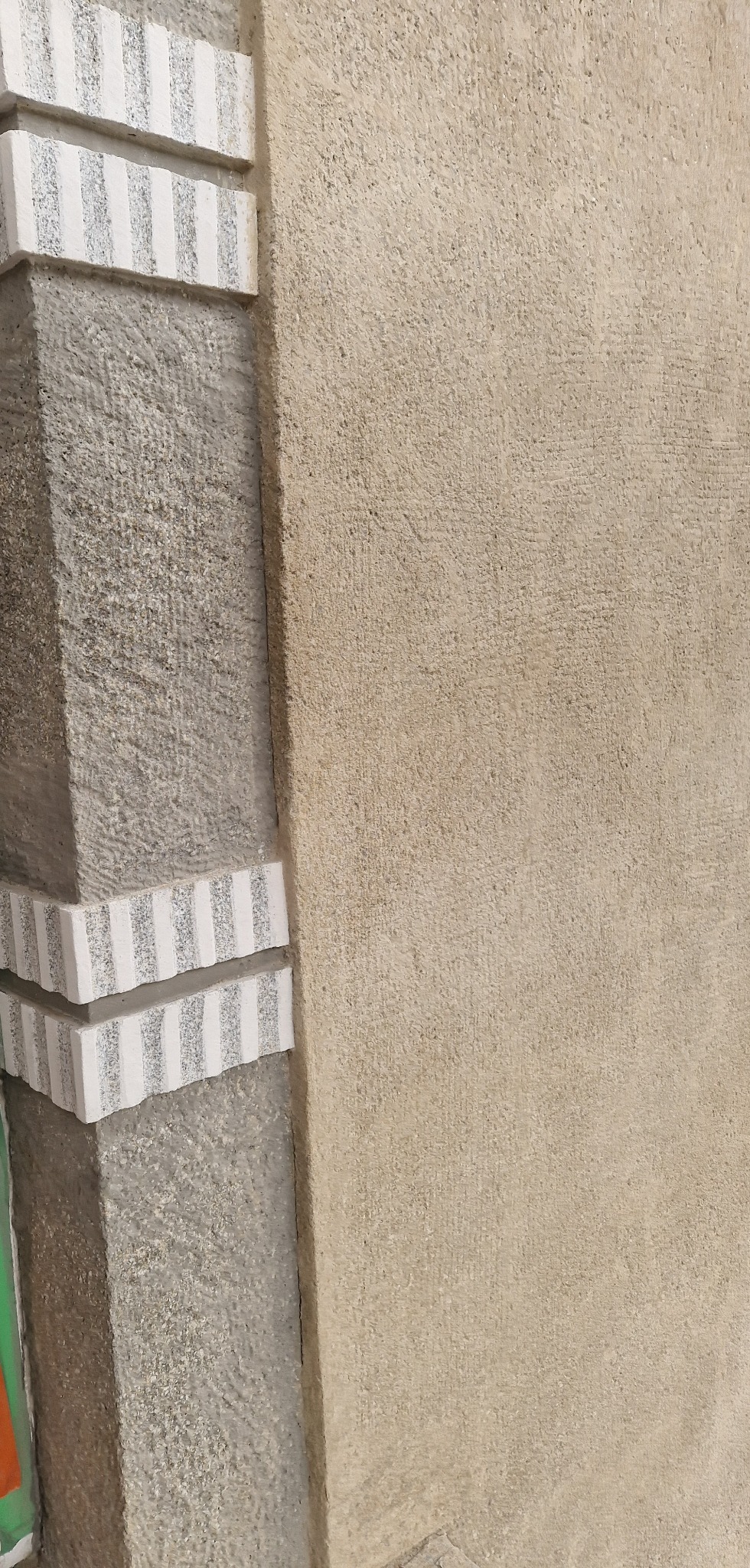 Fragment odnowionej elewacji budynku z kamiennymi elementami dekoracyjnymi. Widoczna struktura kamienia i świeżo pomalowana ściana w odcieniach beżu.