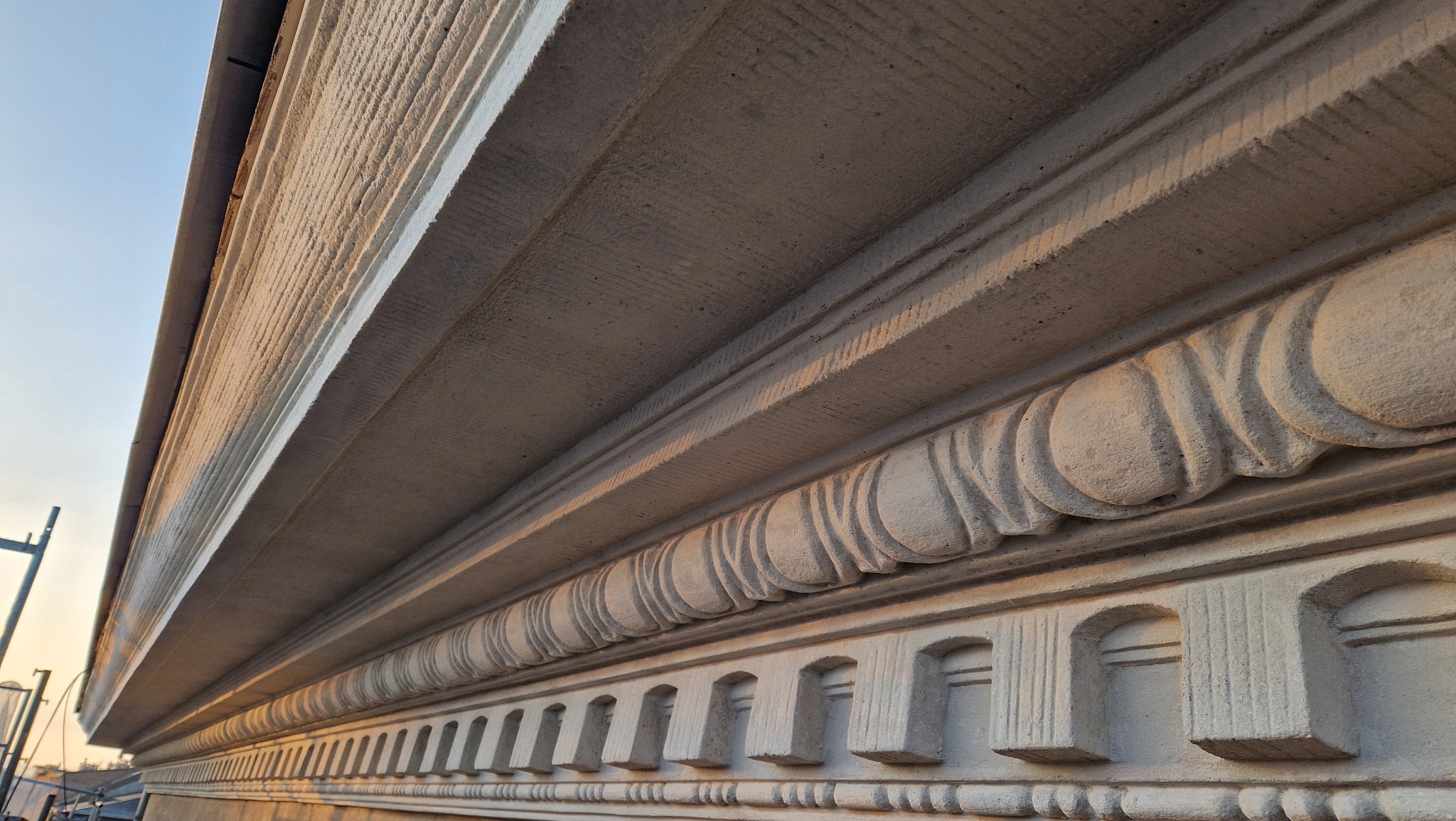 Detal architektoniczny odrestaurowanej fasady budynku z elementami dekoracyjnymi, widoczny pod kątem. Ciepłe światło podkreśla fakturę kamienia.