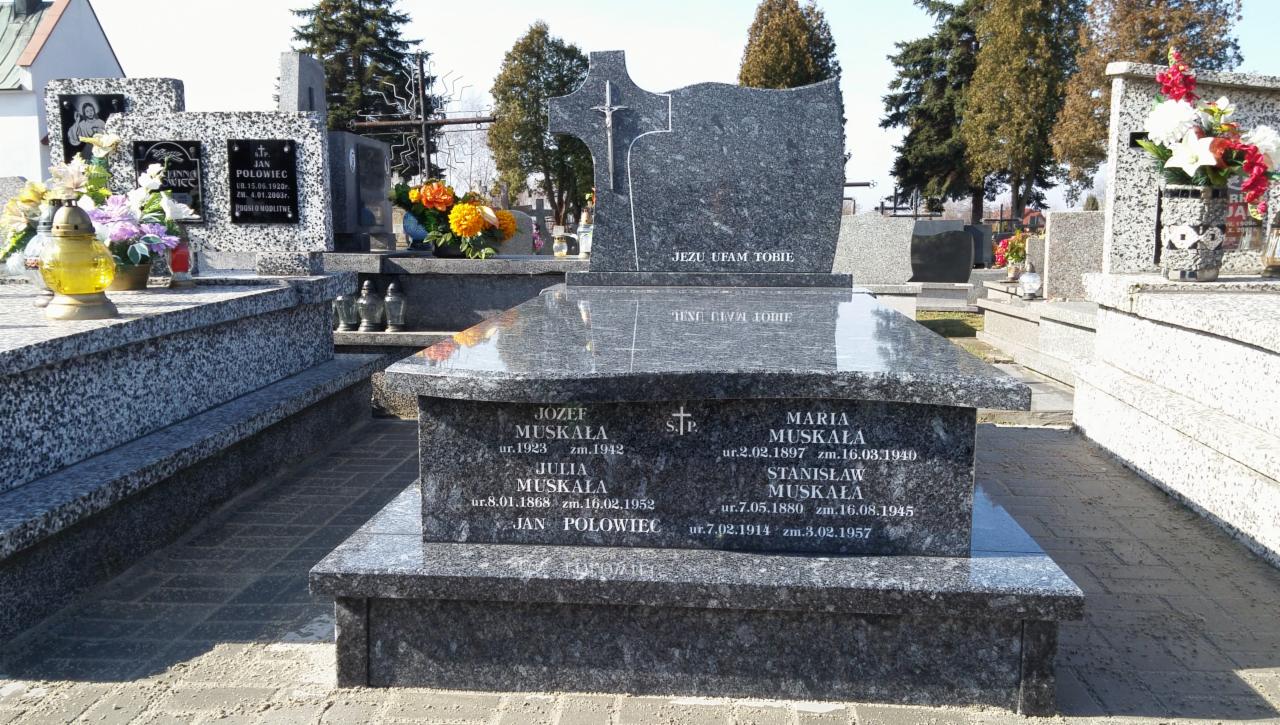 Granitowy pomnik nagrobny z wygrawerowanymi imionami i datami, ozdobiony krzyżem i napisem 'Jezu ufam Tobie', na tle cmentarza.