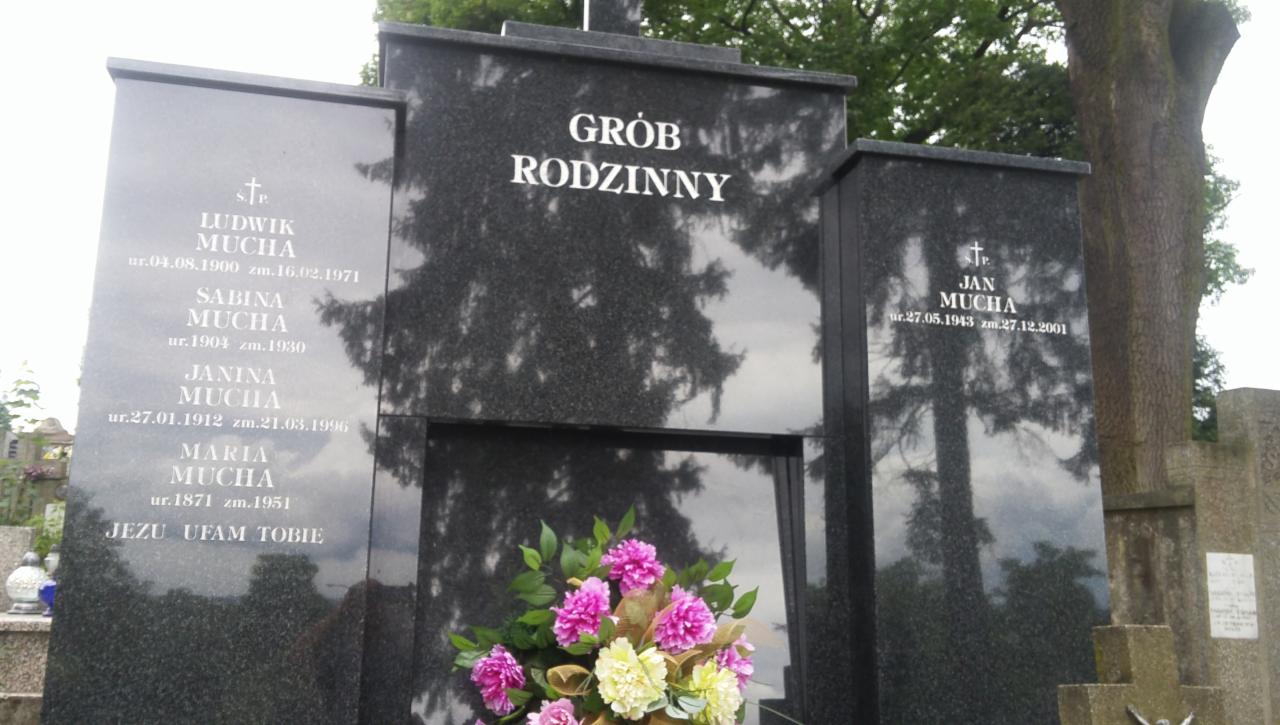 Granitowy nagrobek rodzinny z wygrawerowanymi imionami i datami, ozdobiony bukietem różowych i kremowych kwiatów, na tle drzew