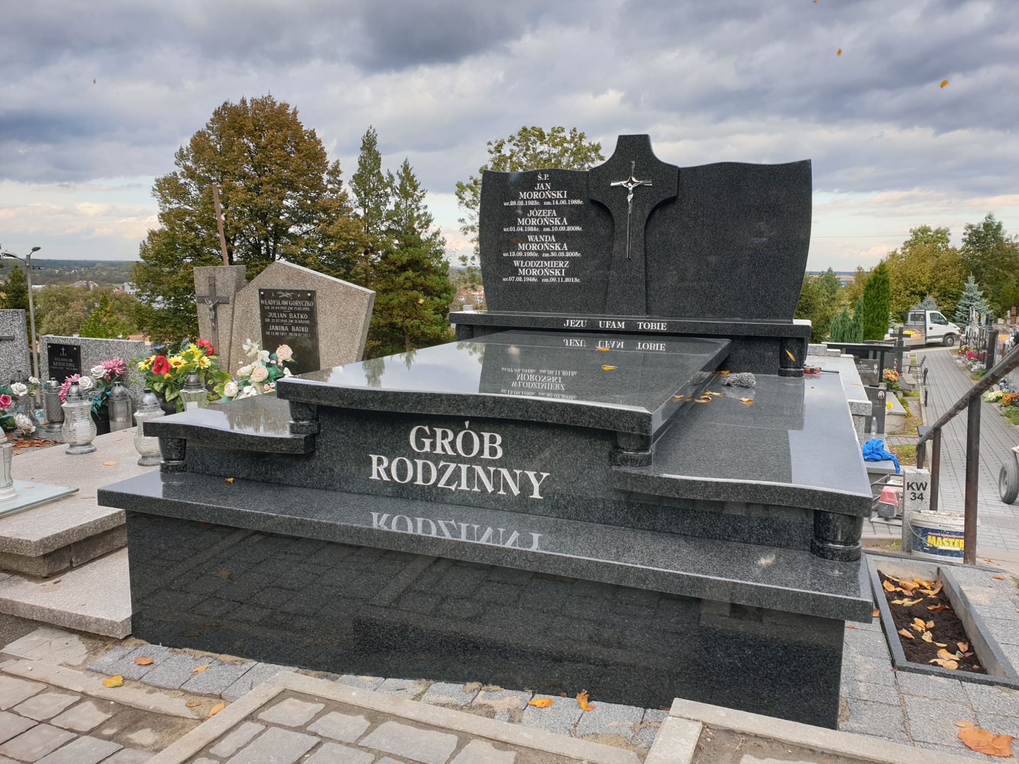 Czarny, granitowy nagrobek rodzinny z inskrypcją 'Grób Rodzinny' na cmentarzu w Bochni, widok z bliska, w tle inne nagrobki i drzewa.