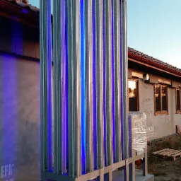 Metalowa konstrukcja z niebieskim podświetleniem na tle budynku w trakcie budowy z widocznym paletą i materiałami budowlanymi.