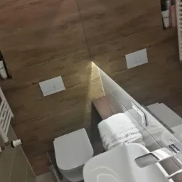 Nowoczesna łazienka po remoncie w Koszalinie: drewnopodobne płytki, biała ceramika sanitarna, minimalistyczna toaleta podtynkowa i umywalka z baterią, odbicie w lustrze.