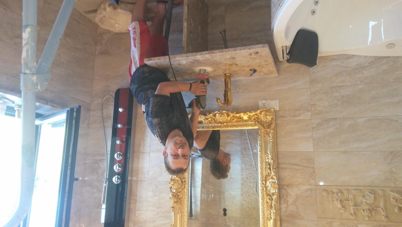 Instalator wierci otwór w marmurowym blacie pod złotą umywalkę w luksusowej łazience z wanną jacuzzi i złotym lustrem.