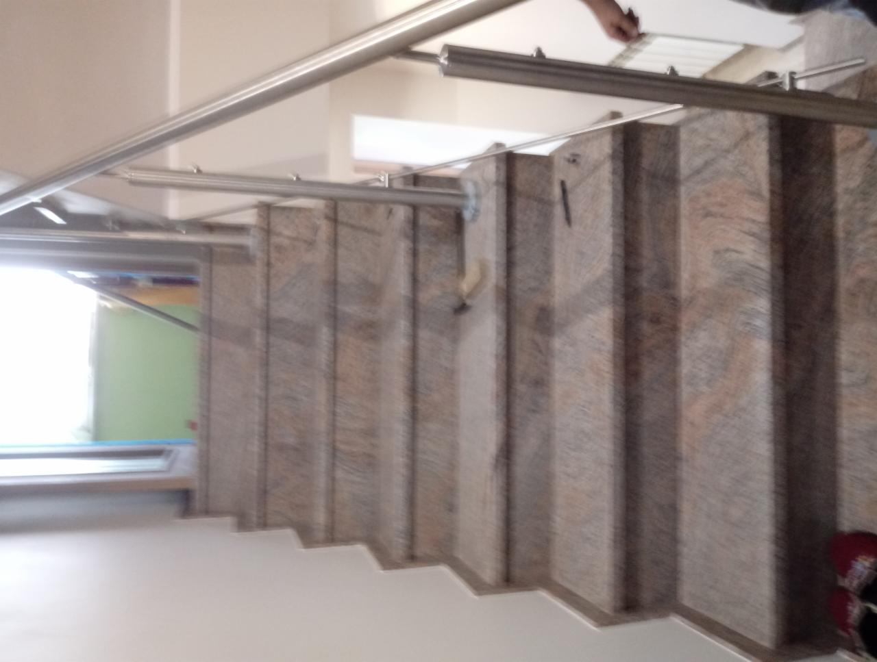 Granitowe schody wewnętrzne z metalową balustradą, widok z góry, jasne wnętrze.