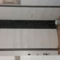 Ściana w trakcie układania płytek, widoczny pas dekoracyjny z ciemnych płytek, przygotowane miejsce na gniazdka elektryczne, zabezpieczona folią część ściany.