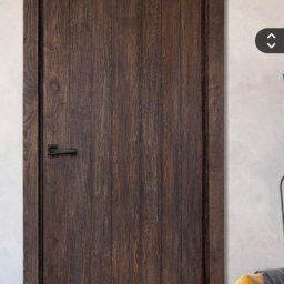 PELIA Włodzimierz Nepelak - Ciemne, drewniane drzwi wewnętrzne z czarną klamką, w rustykalnym stylu. Widoczna faktura drewna i delikatne oświetlenie boczne, podkreślające detale wykończenia.