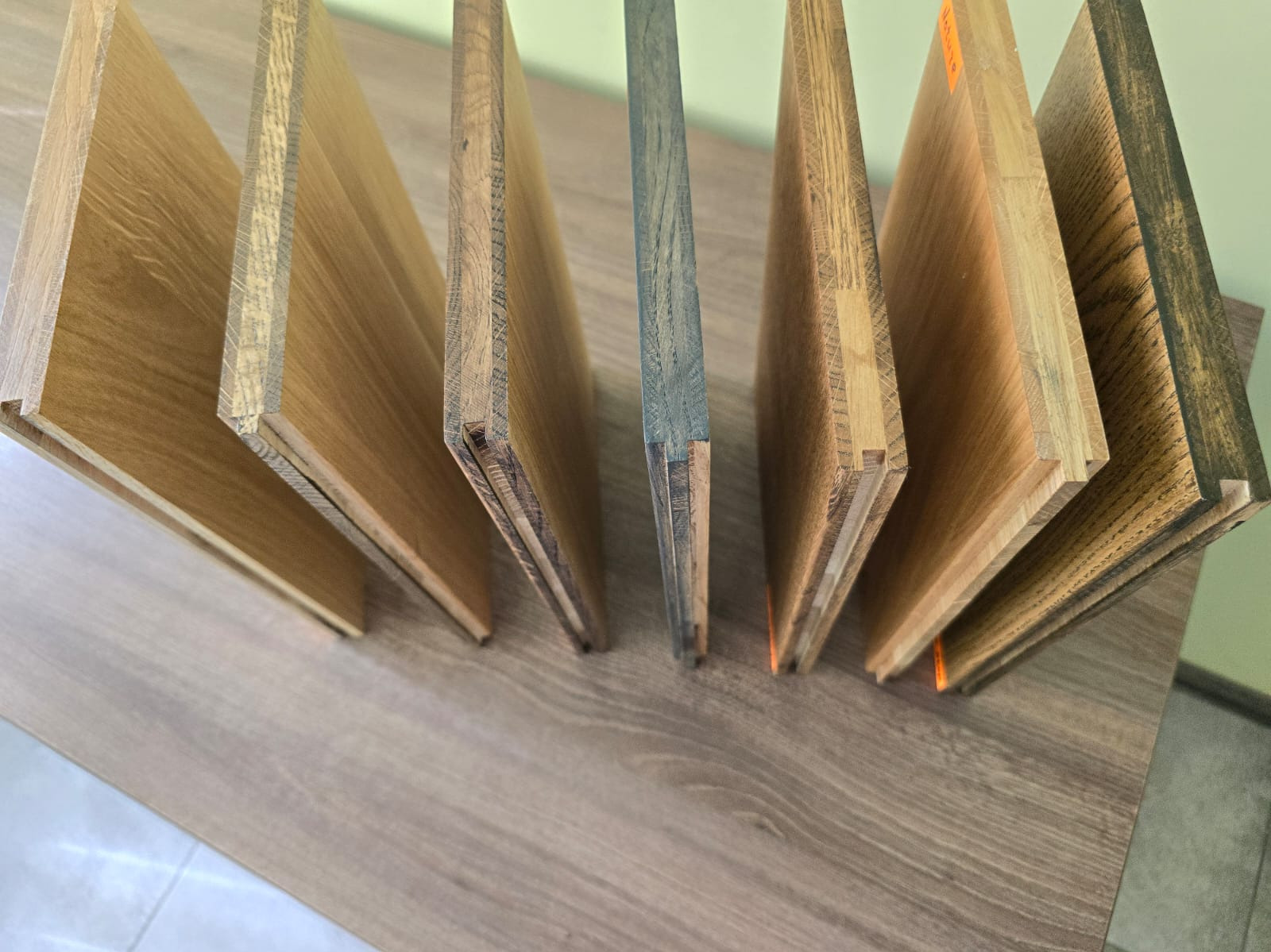 Przekrój różnych odcieni blatów drewnianych z widoczną strukturą drewna i łączeniami, prezentowanych na blacie w ciepłym oświetleniu.