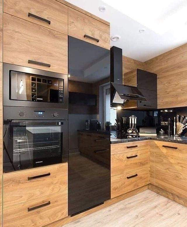 Nowoczesna kuchnia z drewnianymi frontami i czarnymi, lakierowanymi elementami. Zabudowa kuchenna z piekarnikiem, mikrofalówką i okapem.