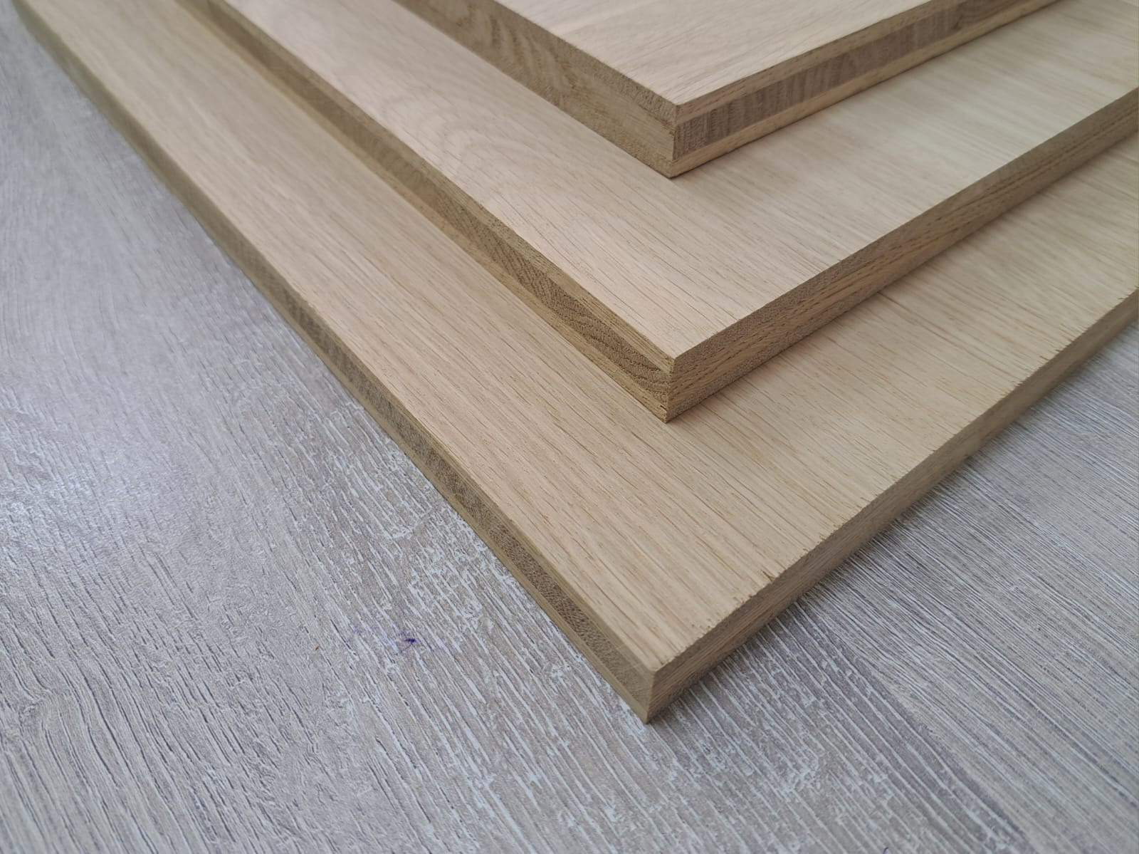 Surowe, jasne blaty drewniane ułożone warstwowo na szarym podłożu. Widoczne krawędzie i naturalny rysunek drewna. Przygotowane do dalszej obróbki.