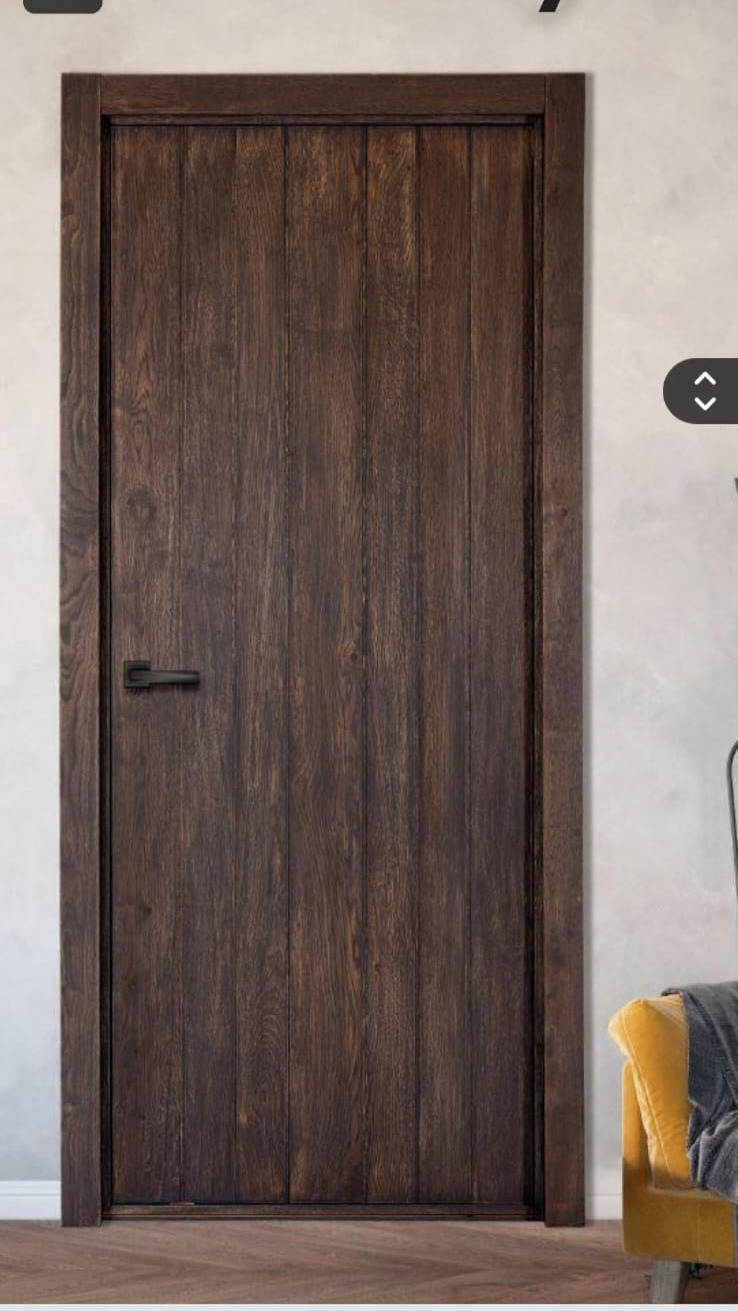 Ciemne, drewniane drzwi wewnętrzne z czarną klamką, w rustykalnym stylu. Widoczna faktura drewna i delikatne oświetlenie boczne, podkreślające detale wykończenia.