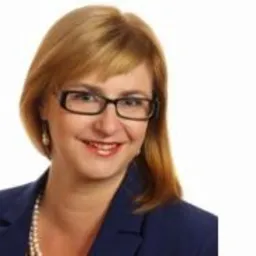 Portret uśmiechniętej kobiety w okularach, blond włosach i niebieskiej marynarce na białym tle.