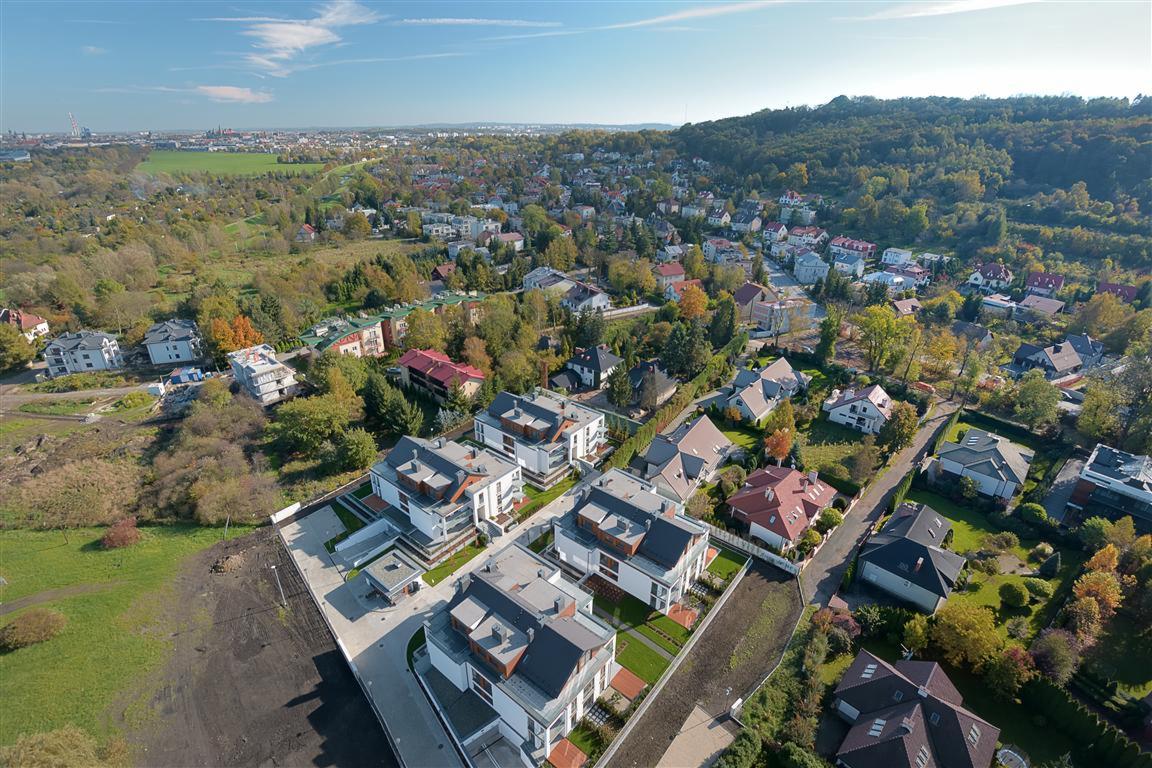 Panorama osiedla nowych domów jednorodzinnych z lotu ptaka, widok na okolicę z zielenią i zabudowaniami.