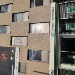 Fasada budynku z oknami, szyldem Crédit Agricole i plakatem reklamującym zdjęcia do dokumentów od 18 zł oraz 39. edycję Rawa Blues Festival w Katowicach.