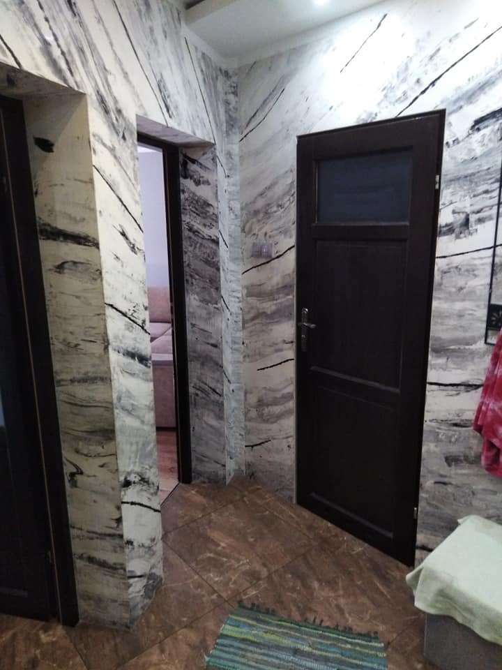 Wnętrze korytarza z dekoracyjnymi ścianami imitującymi marmur, brązowymi drzwiami z przeszkleniem i brązową podłogą z terakoty. W tle widoczny fragment sofy przez otwarte drzwi.