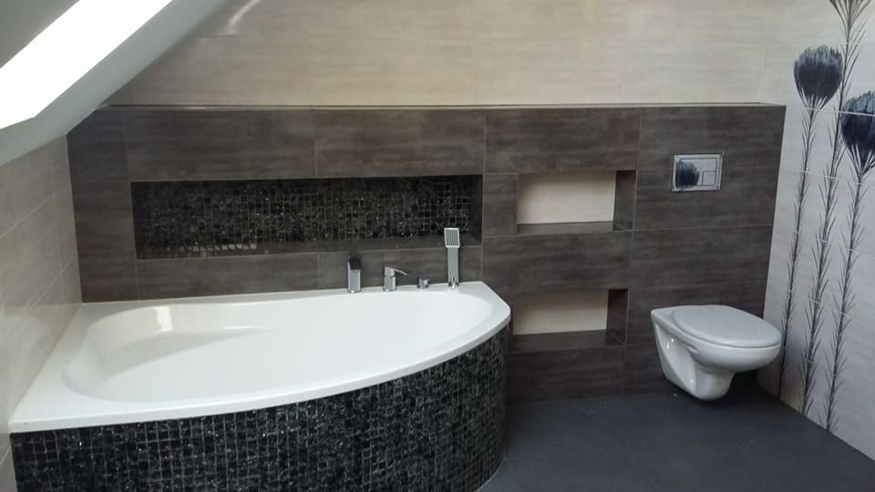 Nowoczesna łazienka na poddaszu z narożną wanną obłożoną czarną mozaiką, szare płytki ścienne z wnękami i wisząca toaleta.