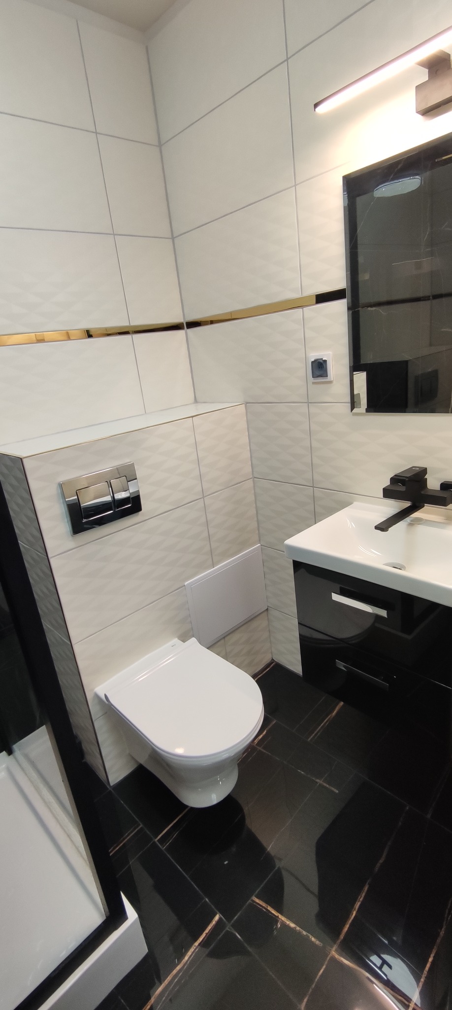 Nowoczesna łazienka z białą armaturą, czarną szafką pod umywalką i podłogą z czarnych płytek imitujących marmur ze złotymi żyłami, ściany wyłożone białymi płytkami z delikatnym wzorem 3D, akcent...