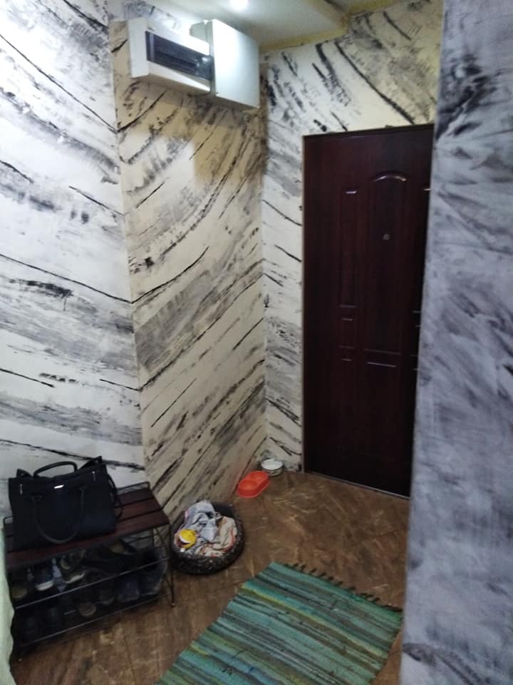 Wnętrze przedpokoju z dekoracyjną ścianą imitującą marmur, ciemnymi drzwiami i wyposażeniem: szafka na buty, torba, legowisko dla zwierząt i dywanik.