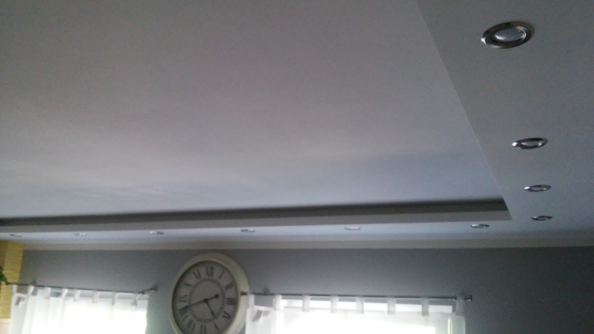 Sufit podwieszany z oświetleniem punktowym LED, widoczny fragment ściany z zegarem w tle.