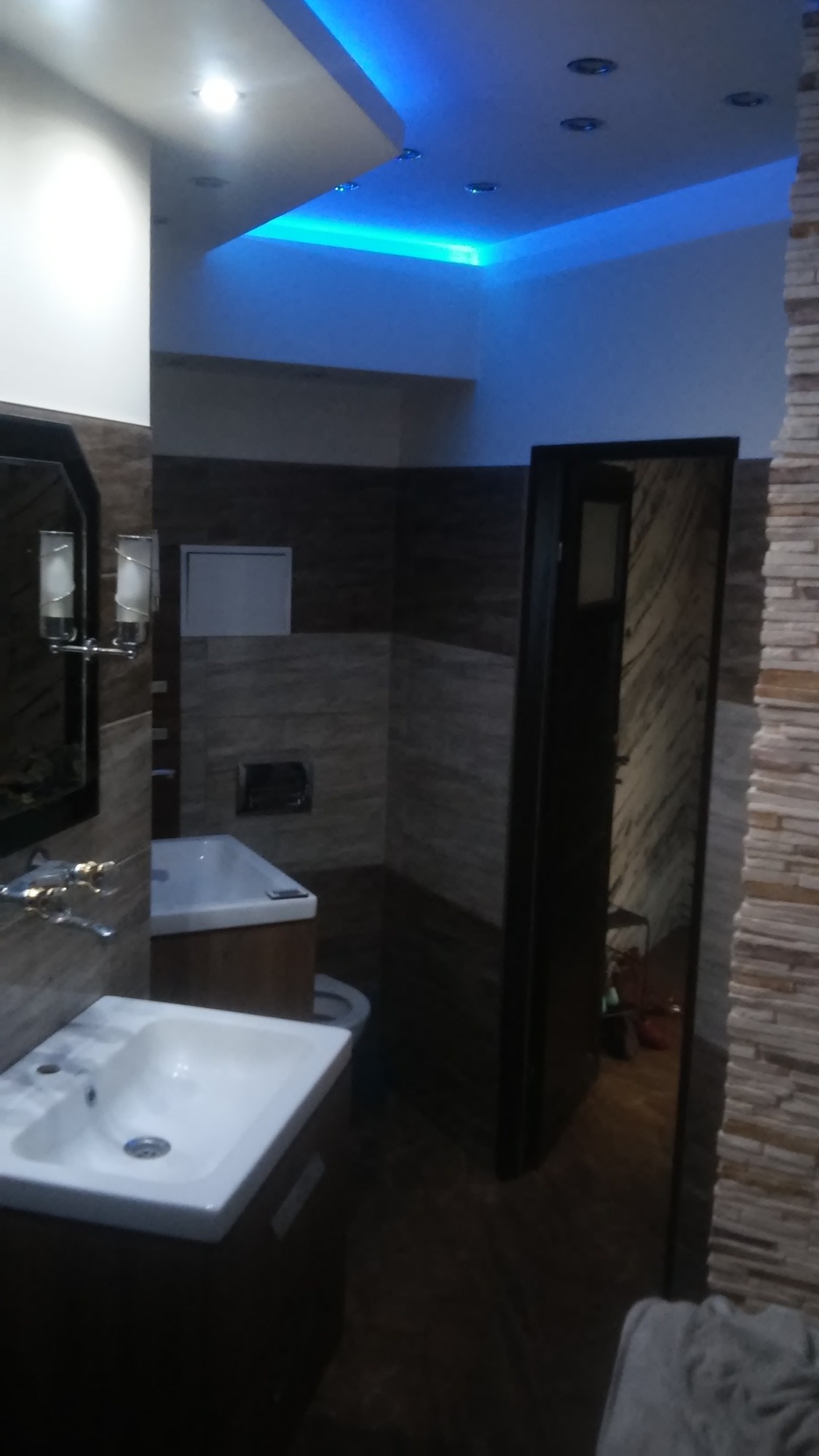 Nowoczesna łazienka z podświetlanym sufitem LED, umywalką nablatową na ciemnej szafce i ścianami wykończonymi w odcieniach brązu i beżu.