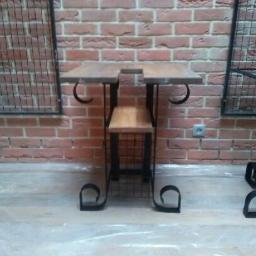 Unistal - Stolik barowy z drewnianym blatem i metalową konstrukcją w stylu industrialnym, na tle ściany z czerwonej cegły i metalowych krat.