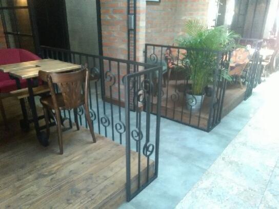 Metalowa balustrada z dekoracyjnymi spiralnymi elementami zabezpieczająca drewniany podest z roślinami doniczkowymi w restauracji.