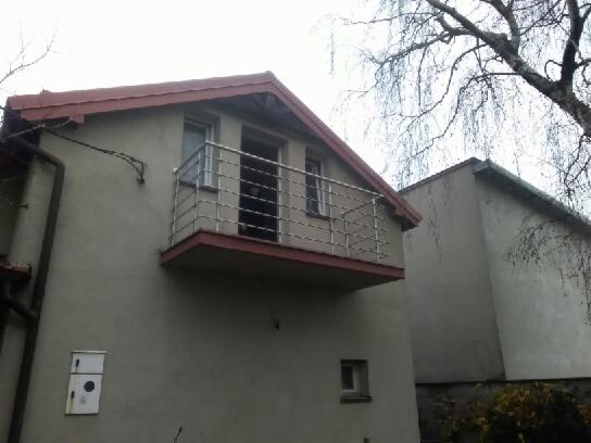 Balkon z balustradą ze stali nierdzewnej w domu jednorodzinnym, widok z dołu, z drzewem w tle.