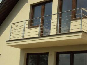 Balkon z nowoczesną, minimalistyczną balustradą ze stali nierdzewnej, z poziomymi prętami, na tle elewacji domu z ciemnymi oknami.