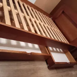 Drewniane łóżko z wysuwanymi szufladami i drewnianym stelażem, widoczne z niskiej perspektywy, ukazujące detale konstrukcji.